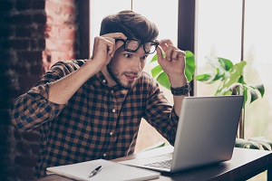 Surprised man raising eyeglasses over head while looking at computer